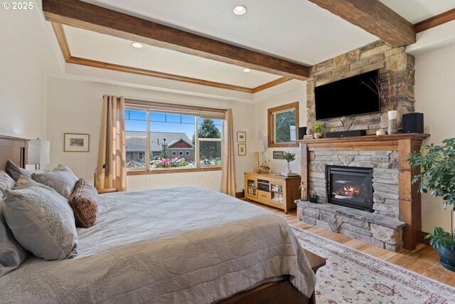 bedroom with beamed ceiling, a fireplace, and wood finished floors