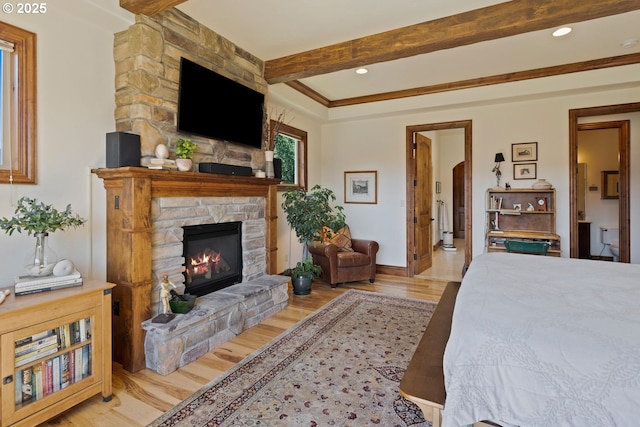 bedroom with a stone fireplace, wood finished floors, baseboards, beamed ceiling, and ensuite bathroom