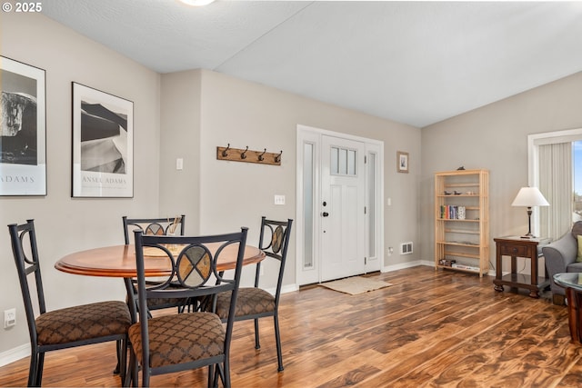 dining space featuring lofted ceiling, wood finished floors, and baseboards