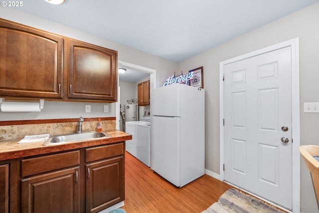 kitchen with light wood finished floors, a sink, light countertops, freestanding refrigerator, and separate washer and dryer