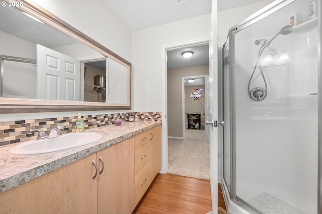 full bath featuring vanity, a shower stall, wood finished floors, and backsplash