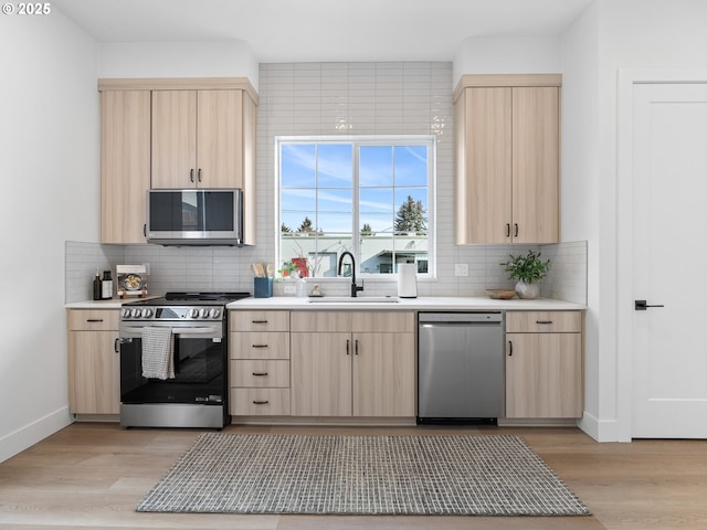 kitchen featuring light wood-type flooring, stainless steel appliances, sink, backsplash, and light brown cabinets