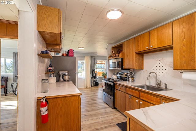 kitchen with stainless steel appliances, a sink, light wood-type flooring, brown cabinets, and open shelves