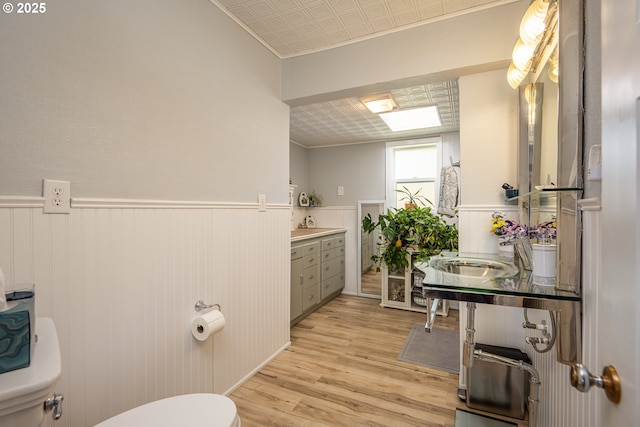 bathroom with toilet, wood finished floors, a sink, wainscoting, and an ornate ceiling