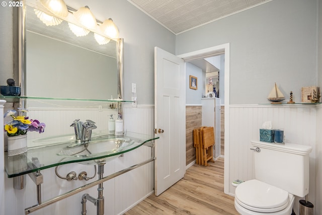 bathroom featuring an ornate ceiling, toilet, wainscoting, a sink, and wood finished floors