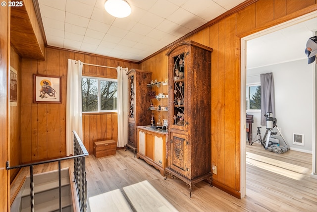 interior space with wooden walls, visible vents, ornamental molding, and light wood-style flooring