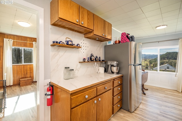 kitchen with tasteful backsplash, brown cabinets, freestanding refrigerator, light wood-style floors, and open shelves