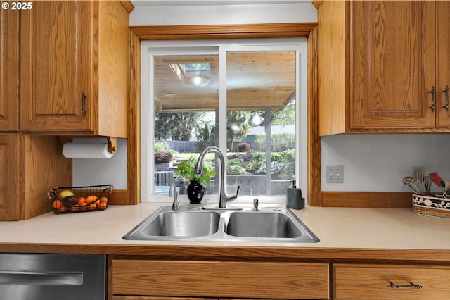 kitchen featuring stainless steel dishwasher, a sink, brown cabinets, and light countertops