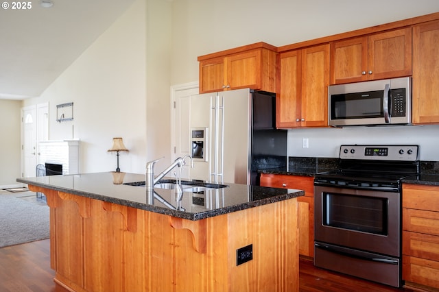 kitchen with lofted ceiling, sink, appliances with stainless steel finishes, an island with sink, and dark stone counters