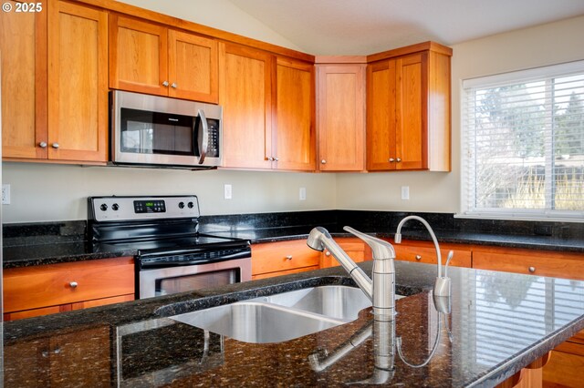 kitchen featuring lofted ceiling, appliances with stainless steel finishes, sink, and dark stone counters