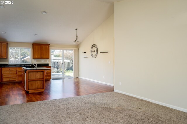 kitchen featuring sink, dark colored carpet, a center island with sink, decorative light fixtures, and vaulted ceiling