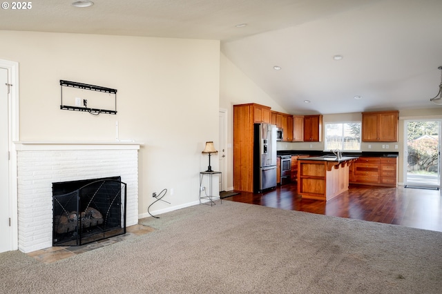 kitchen featuring stainless steel appliances, a center island, a kitchen breakfast bar, a brick fireplace, and dark carpet