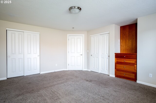 unfurnished bedroom featuring carpet floors, a textured ceiling, and two closets