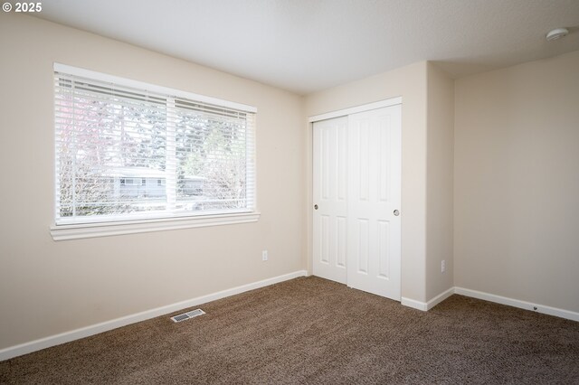 unfurnished bedroom with dark carpet and a closet