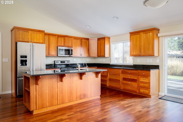 kitchen with lofted ceiling, stainless steel appliances, a breakfast bar, and a center island with sink