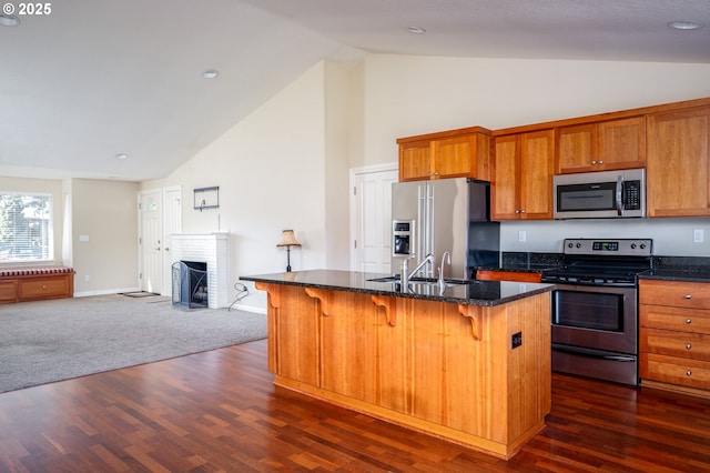 kitchen featuring a kitchen island with sink, stainless steel appliances, a kitchen breakfast bar, a fireplace, and dark stone counters