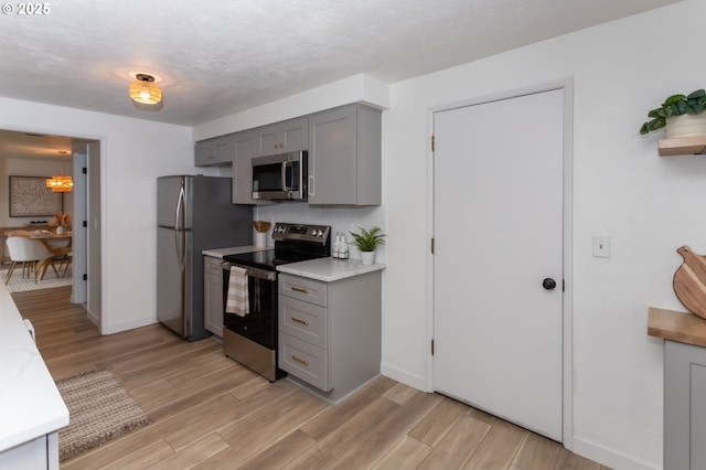 kitchen with light countertops, light wood finished floors, gray cabinets, and appliances with stainless steel finishes