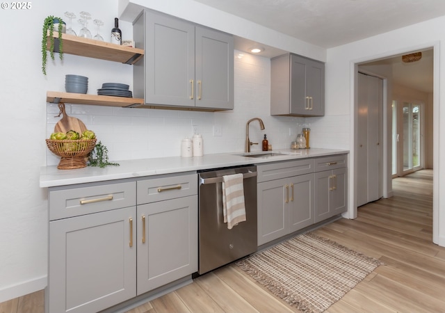 kitchen featuring light wood-type flooring, gray cabinets, a sink, backsplash, and dishwasher