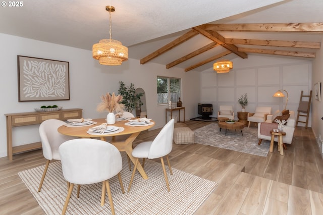 dining space with light wood-type flooring, vaulted ceiling with beams, an inviting chandelier, and a wood stove