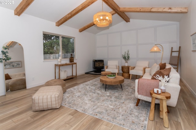 living area with lofted ceiling with beams, a notable chandelier, wood finished floors, and a wood stove