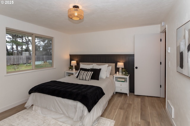 bedroom with baseboards, light wood finished floors, and a textured ceiling