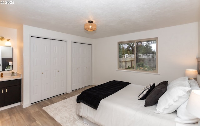 bedroom featuring a textured ceiling, multiple closets, and light wood-type flooring