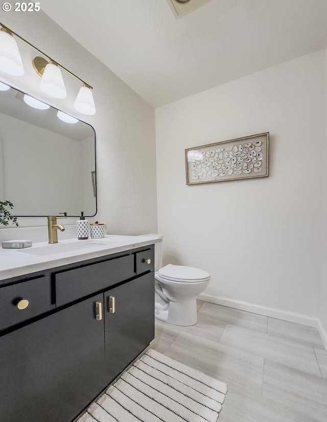 half bath with baseboards, toilet, and vanity