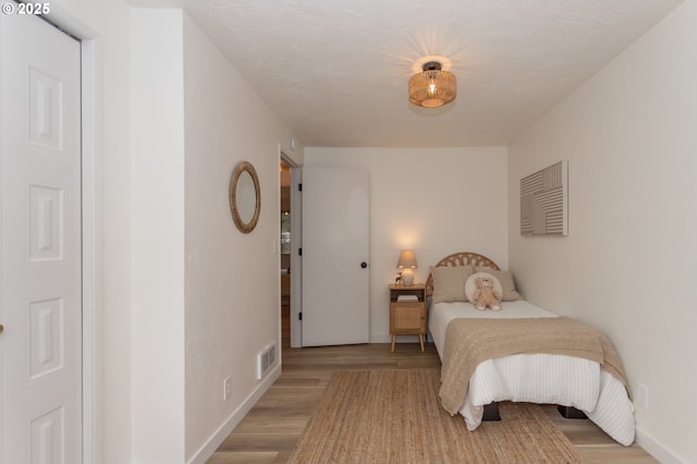 bedroom with visible vents, a textured ceiling, light wood-type flooring, and baseboards