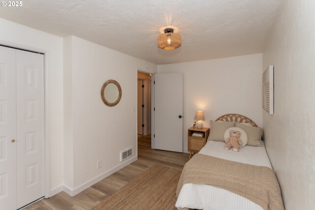 bedroom with light wood-type flooring, visible vents, baseboards, and a textured ceiling