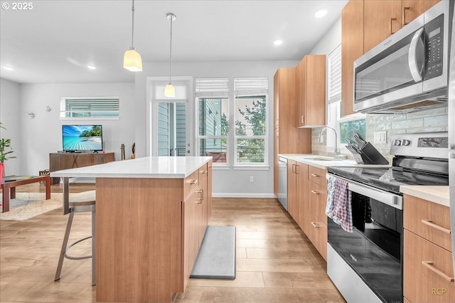 kitchen with a sink, stainless steel appliances, light wood-type flooring, light countertops, and a kitchen island