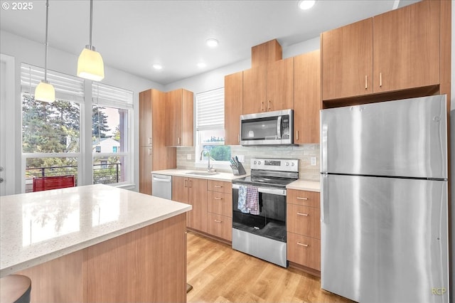 kitchen with a sink, tasteful backsplash, pendant lighting, light wood-style flooring, and appliances with stainless steel finishes