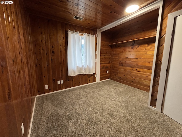 unfurnished room with wood ceiling, wooden walls, visible vents, and carpet flooring