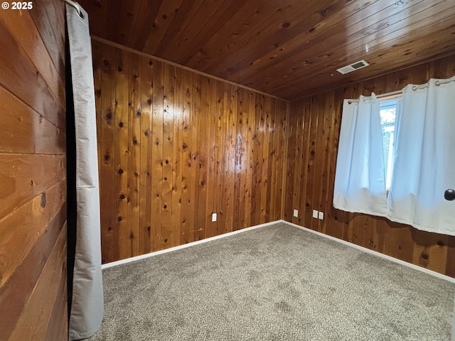 carpeted empty room featuring wood ceiling, wooden walls, visible vents, and baseboards