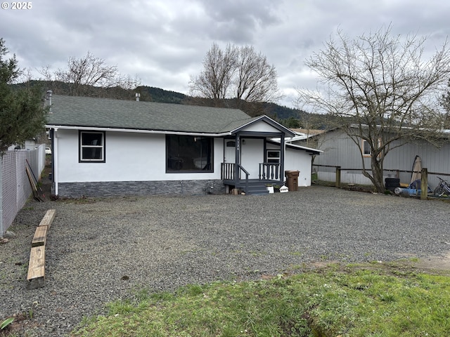 view of front facade featuring driveway, stucco siding, a fenced backyard, and roof with shingles