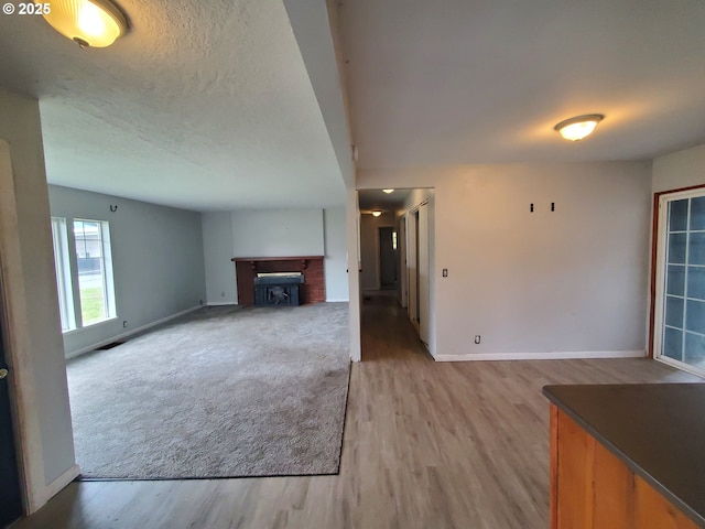 unfurnished living room with a fireplace, a textured ceiling, baseboards, and wood finished floors