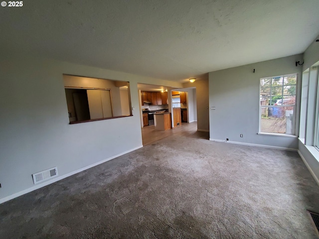 unfurnished living room featuring baseboards, visible vents, and carpet flooring