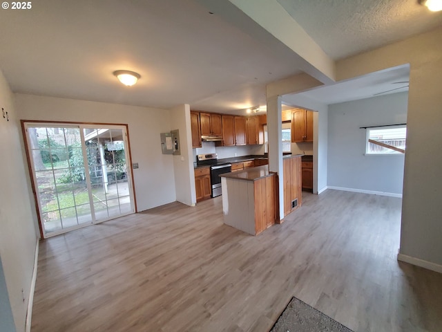 kitchen featuring under cabinet range hood, a healthy amount of sunlight, stainless steel electric range oven, light wood finished floors, and dark countertops