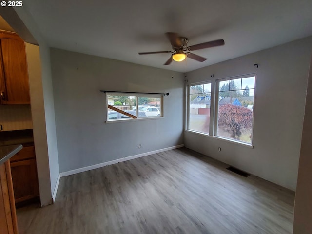 interior space featuring visible vents, ceiling fan, light wood-style flooring, and baseboards