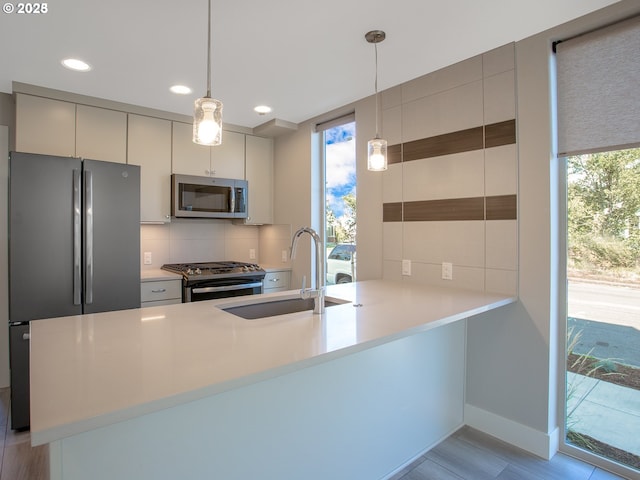 4984 NE 32nd Pl, Portland, OR 97211 - kitchen featuring appliances with stainless steel finishes, a sink, backsplash, a peninsula, and light countertops