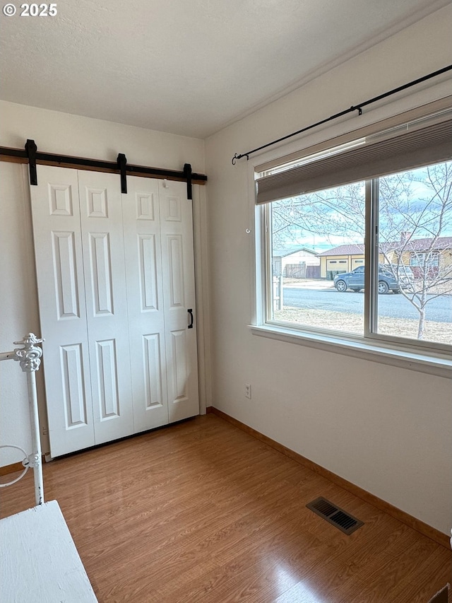 unfurnished bedroom featuring visible vents, baseboards, a barn door, wood finished floors, and a closet