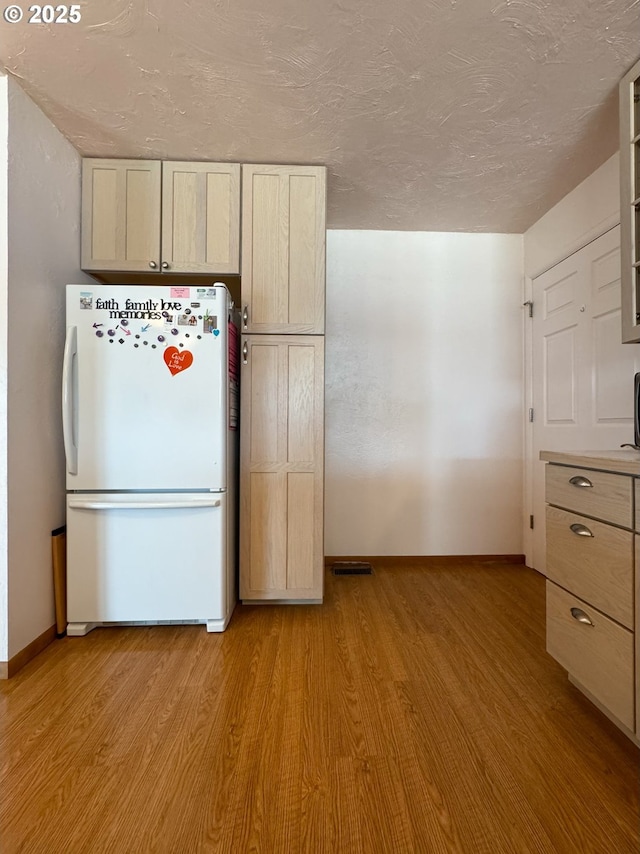 kitchen featuring glass insert cabinets, a textured ceiling, freestanding refrigerator, and light wood-style floors