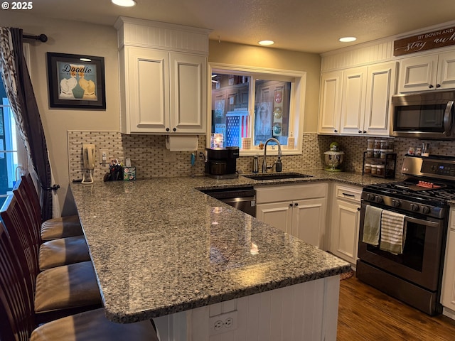 kitchen with stone counters, sink, white cabinets, a kitchen bar, and stainless steel appliances