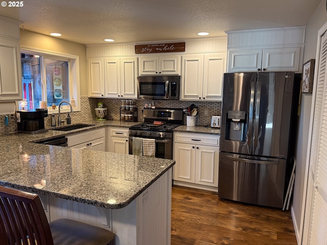 kitchen with a breakfast bar, sink, white cabinetry, stone countertops, and stainless steel appliances