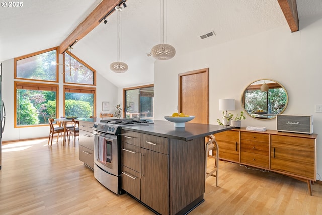 511 SW Colony Dr, Portland, OR 97219 - kitchen featuring stainless steel range with gas stovetop, light wood-type flooring, dark countertops, a kitchen island, and a kitchen breakfast bar