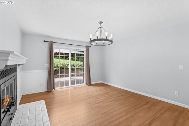 21689 SW Klickitat Ct, Tualatin, OR 97062 - unfurnished living room featuring a fireplace, a chandelier, light wood-type flooring, a wainscoted wall, and baseboards