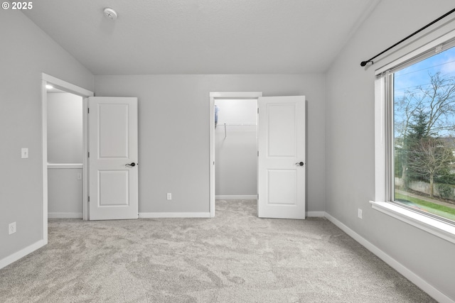 unfurnished bedroom featuring a walk in closet, light colored carpet, and a closet