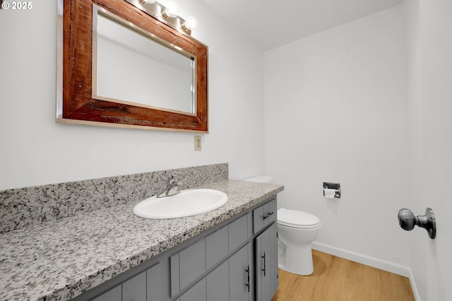 half bath featuring baseboards, vanity, toilet, and wood finished floors