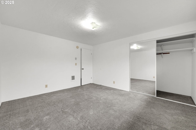 unfurnished bedroom with a closet, visible vents, dark carpet, and a textured ceiling