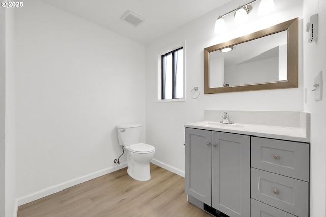 bathroom featuring baseboards, visible vents, toilet, wood finished floors, and vanity