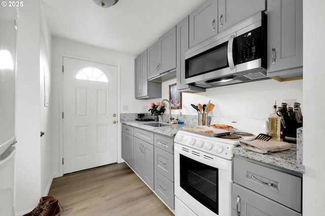 kitchen featuring white electric range oven, light wood-style flooring, stainless steel microwave, light stone countertops, and a sink